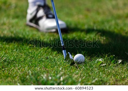 Male foot with iron golf club and golf ball on green grass.
