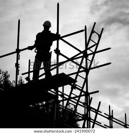 silhouette of construction worker against sky on scaffolding with ladder on building site.Monochrome
