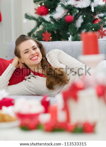 Happy young woman laying on couch near Christmas tree