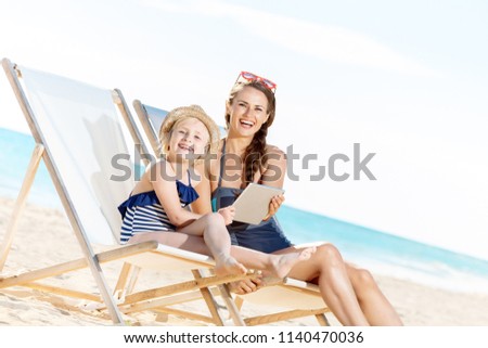 smiling modern mother and child in swimwear on the seashore using tablet PC while sitting on beach chairs Foto stock © 