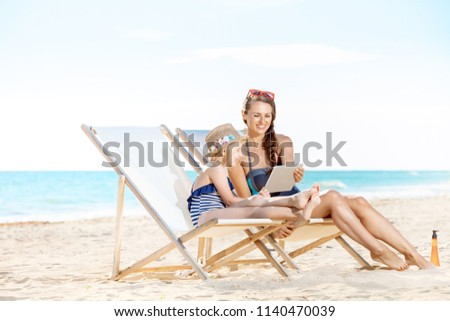 smiling young mother and child in swimwear on the seashore using tablet PC while sitting on beach chairs Foto stock © 