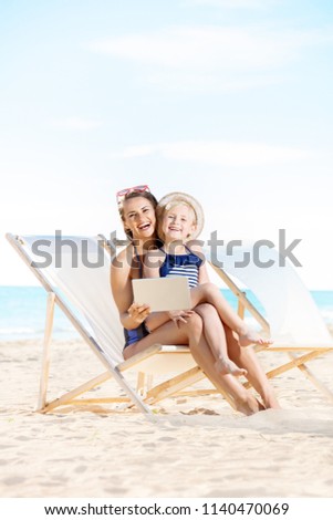 happy young mother and child in swimsuit on the seashore using tablet PC while sitting on beach chairs Foto stock © 