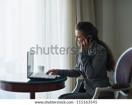 Business woman working on laptop and speaking mobile in hotel room