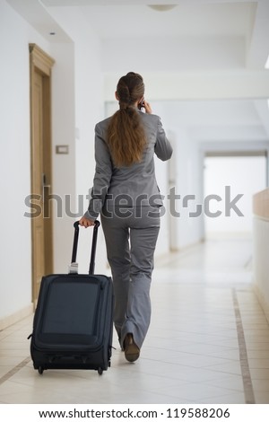 Business woman in business trip with wheel bag. Rear view