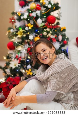 Portrait of happy young woman sitting near Christmas tree