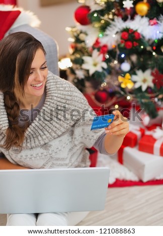 Smiling woman with laptop and credit card near Christmas tree