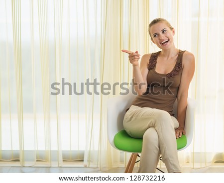 Smiling young woman sitting on modern chair and pointing on copy space