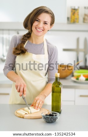 Smiling young housewife cutting fresh cheese