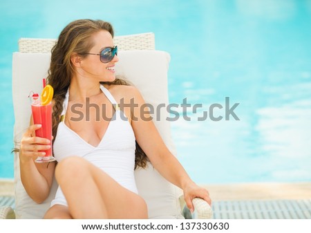 Happy young woman with cocktail laying on chaise-longue and looking on copy space
