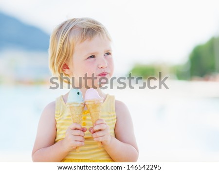 Happy baby eating two ice cream horns and looking on copy space