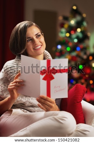 Young woman with christmas postcard in front of christmas tree
