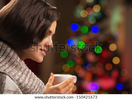 Happy young woman with cup of hot chocolate in front of christmas lights