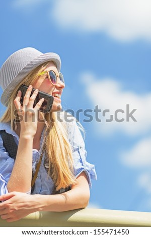 Smiling hipster girl talking mobile phone and looking on copy space against sky
