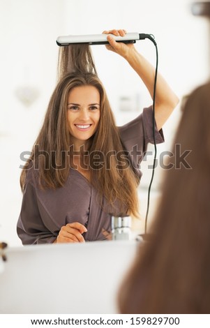 Portrait of happy woman straightening hair with straightener