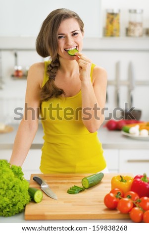 Happy young woman biting cucumber while cutting fresh salad