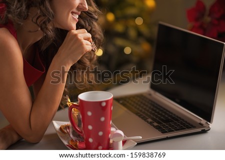 Closeup on young woman having christmas cookies with cup of hot chocolate and usign laptop