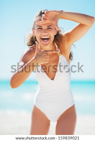 Smiling young woman framing with hands on beach