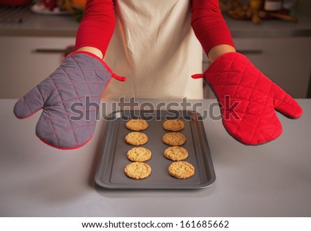 Closeup on kitchen gloves showing by young housewife and christmas cookies on pan