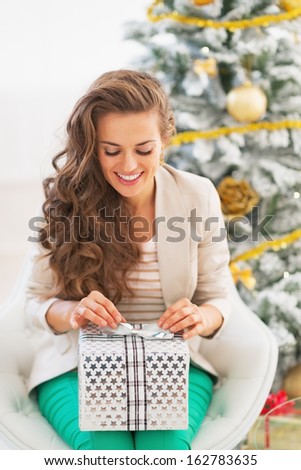 Smiling young woman opening christmas present box in front of christmas tree