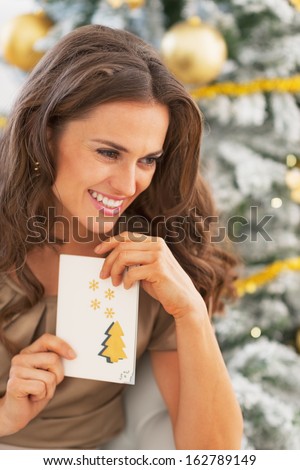 Portrait of happy young woman and christmas postcard near christmas tree