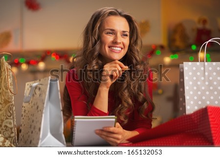 Happy young woman with shopping bags in christmas decorated kitchen checking list of gifts