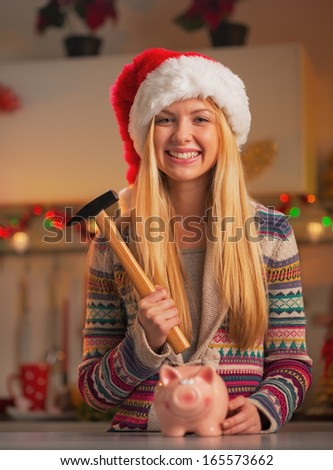 Portrait of smiling teenage girl in santa hat with hammer and piggy bank in christmas decorated kitchen
