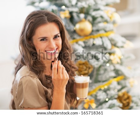 Happy young woman eating candy with latte macchiato near christmas tree
