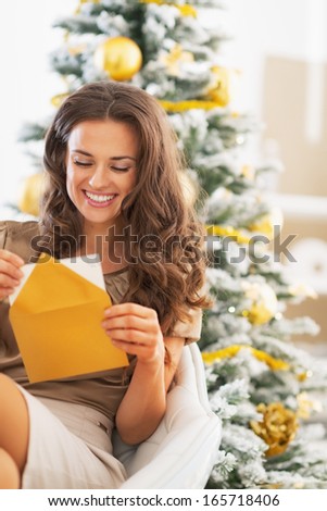 Happy young woman opening christmas letter near christmas tree