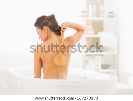 Young woman washing with body brush in bathtub