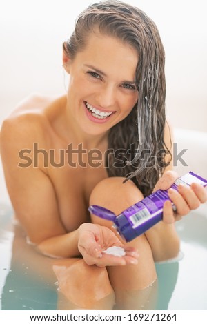 Happy young woman applying hair mask in bathtub
