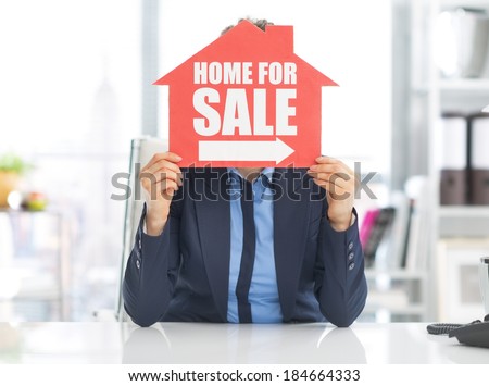 Realtor woman holding home for sale sign in front of face