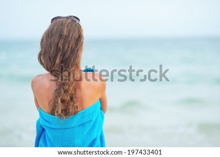 Young woman in towel on beach looking into distance. rear view