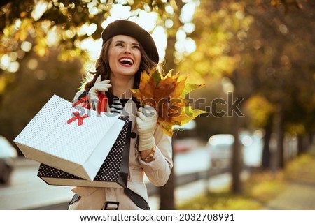 Hello november. happy elegant middle aged woman in beige trench coat and black beret with shopping bags and autumn yellow leaves outside on the city street in autumn. Foto d'archivio © 