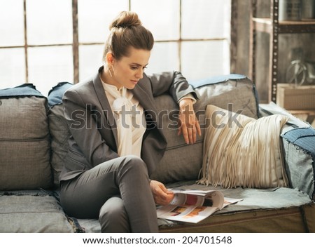 Relaxed business woman sitting on sofa in loft apartment and looking magazine