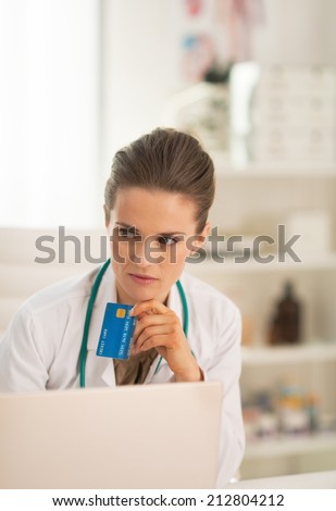 Portrait of thoughtful doctor woman with credit card
