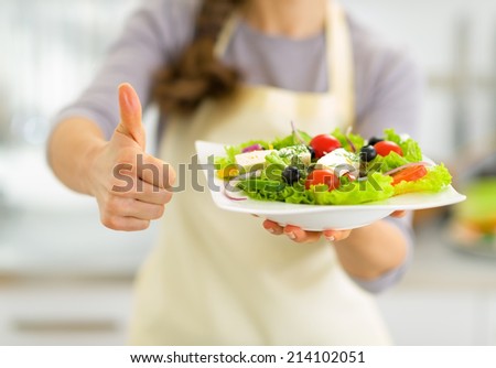 Closeup on young housewife showing greek salad and thumbs up