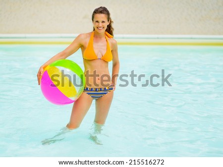 Portrait of young woman with ball standing in swimming pool