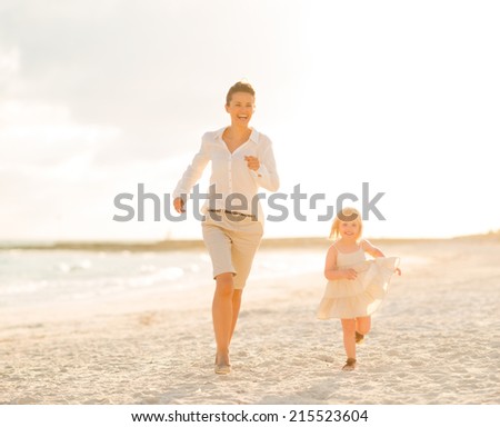 Mother and baby girl running on the beach in the evening