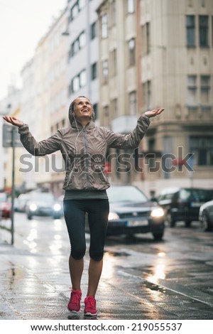 Full length portrait of happy fitness young woman catching rain drops in the city