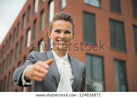 Portrait of happy business woman stretching hand for handshake in front of office building