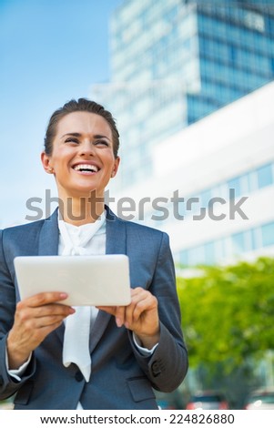 Happy business woman using tablet pc in front of office building