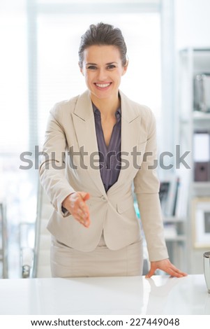 Portrait of happy business woman stretching hand for handshake in office