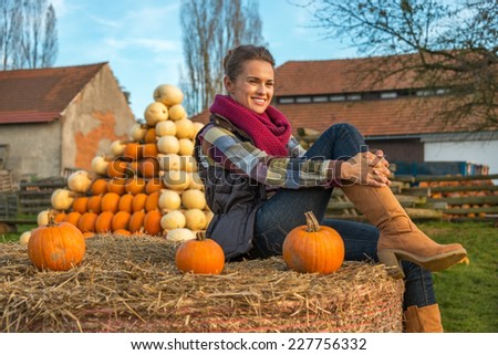Portrait of young woman sitting on haystack with pumpkin in front of pumpkin piramide