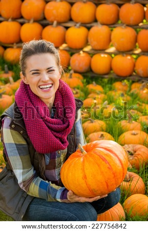Portrait of happy young woman holding pumpkin in front of pumpkin rows