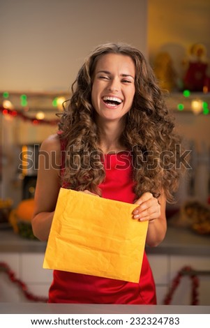 Smiling young housewife opening envelope in christmas decorated kitchen