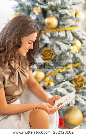 Happy young woman with christmas postcard sitting near christmas tree