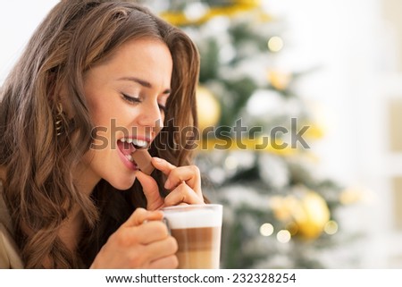 Young woman eating candy with latte macchiato near christmas tree