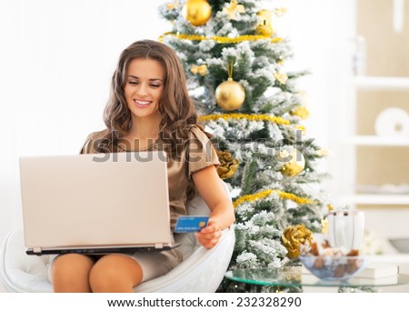 Happy young woman with credit card using laptop near christmas tree