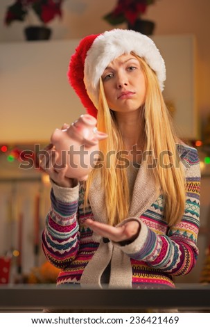 Portrait of displeased teenager girl in santa hat with piggy bank