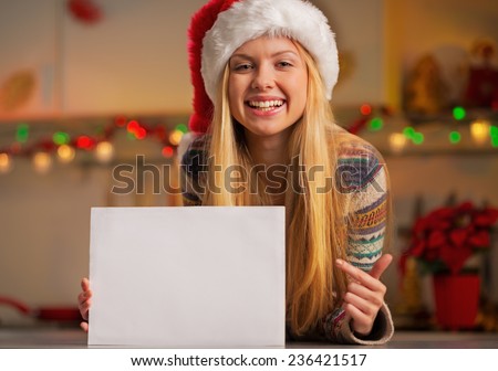 Happy teenager girl in santa hat showing blank paper sheet